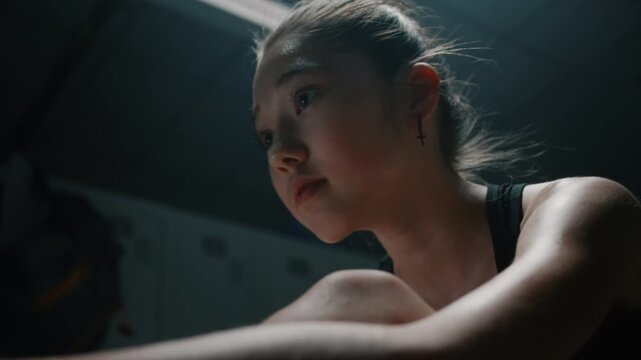 Young Female Competitor Recovering Mentally From Physical Fatigue on Locker Room Bench. Sitting in Dark Girl Reflects on Goals. Concept of Painful Side of Professional Sports Preparation, Loneliness.