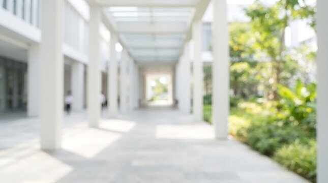 Blurred outdoor corridor walkway in modern office building with white pillars and lush green garden view for architectural background design and commercial real estate presentations