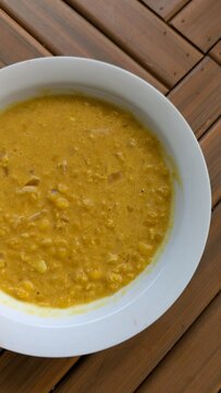 Closeup topdown fresh homemade Sri Lankan lentil dhal curry in white bowl displayed on wooden table