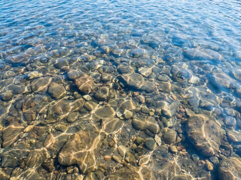 Natural water surface with gentle waves and visible stones under bright sunlight.