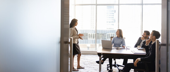 Naklejka premium Businesswoman presenting project details to multiethnic colleagues sitting at conference table in meeting room, banner. Concept of business strategy planning, management briefing, corporate teamwork
