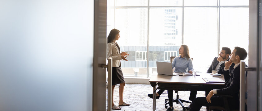 Businesswoman presenting project details to multiethnic colleagues sitting at conference table in meeting room, banner. Concept of business strategy planning, management briefing, corporate teamwork