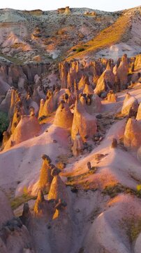 Vertical video. Goreme, Nevsehir, Turkey. Devrent Valley fairy chimneys and hoodoo rock formations, aerial panoramic view at golden hour over the eroded volcanic landscape. Aerial View. Rich colors