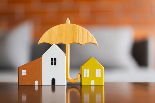 Home insurance protection concept with wooden umbrella covering family model houses for property coverage, real estate investment safety, risk and mortgage loan.