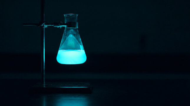 Chemistry experiment with glowing blue liquid in Erlenmeyer flask on laboratory stand, dark scientific research lab, discovery concept.