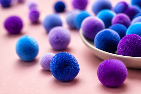 Colorful pom-poms of various sizes are scattered on a pink surface.