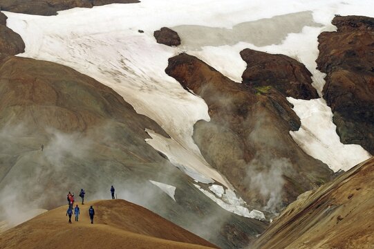 People on a hiking trail in front of snowfields, Geothermal landscapes and steam from hot springs, Kerlingarfjell, Iceland