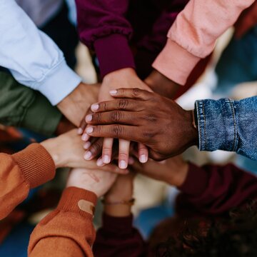 Diverse hands stacked together in a circle, featuring high-contrast skin tones and colorful sleeves for community and collaborative teamwork concepts