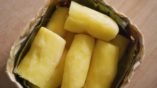Close up video of Indonesian fermented cassava, locally known as Tape / Tapai Singkong, served in a traditional woven bamboo basket on a wooden table background.