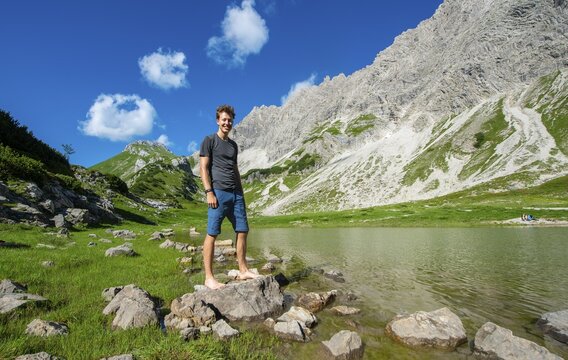 Young man stands on stone, mountain lake at Prinz-Luitpold-Haus, Allg&auml;u Alps, Bad Hindelang, Allg&auml;u, Bavaria, Germany