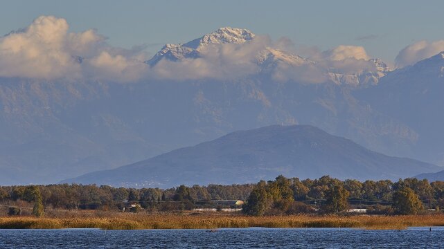 Snow-capped mountain peaks rise behind a landscape with water, Strofilia biotope, wetlands, Kalogria, Peloponnese, Greece