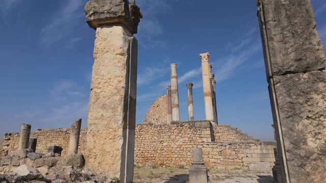 Ground-level view of the ancient Roman temple at the UNESCO-listed Volubilis archaeological site in Morocco, featuring preserved stone columns and classical architecture.