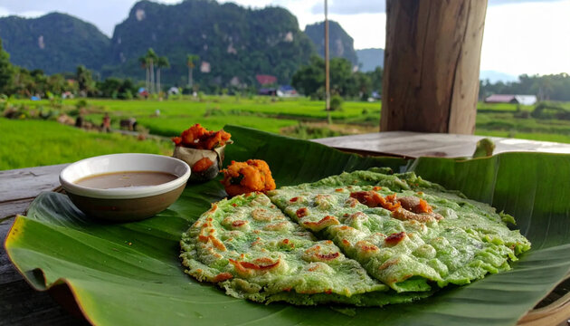 Fresh Indonesian pancake served on a green banana leaf with savory dipping sauce overlooking lush rolling green rice terraces and tropical mountains under a bright sunny daytime summer sky