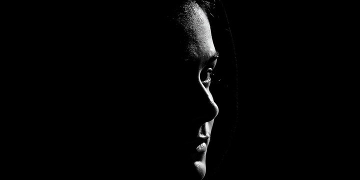 A portrait of a person's face in profile, dramatically lit by a single light source against a dark background. The lighting creates strong contrasts.