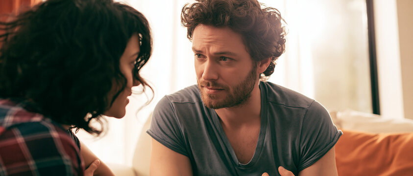 A man and a woman having an intense conversation, with the man gesturing with his hands and looking directly at the woman, who is looking back with a serious expression