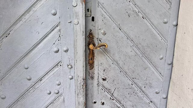Weathered gray historical wooden double door with an aged copper lock and matching handle. Rustic architectural detail showcasing vintage craftsmanship, textured wood, and timeless heritage design