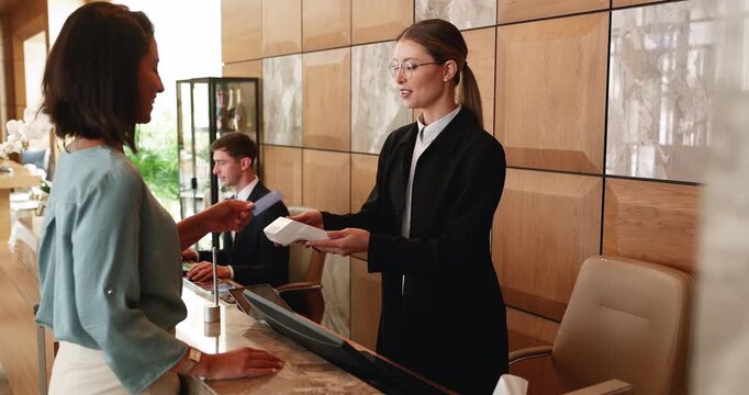 Brazilian female, hotel guest finalizes her check-in by tapping card on terminal, completing payment, collects her keycard, leaving reception area. Travel, customer satisfaction, luxury accommodation