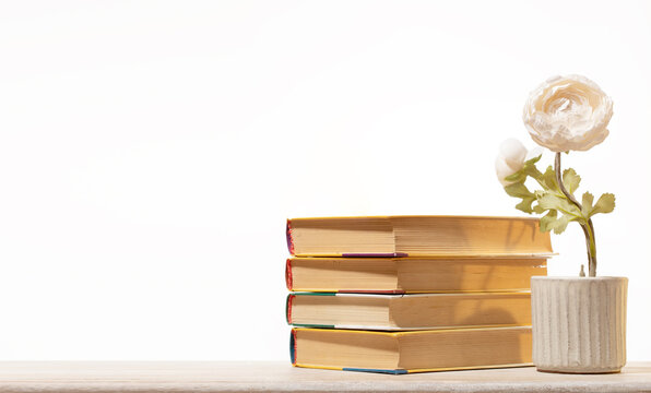 Stack of four vintage books on wooden surface next to a delicate white artificial flower in a textured grey pot. Minimalist background creates a sense of calm and clarity