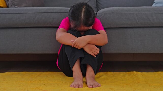 Depressed young girl embracing her knees on carpet hiding face at home