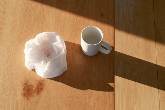 White fabric wrap resting on light oak table in warm morning sunlight with clean minimalist shadow and empty space