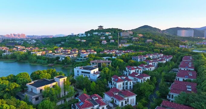 High angle view of a luxury residential community surrounded by lush green trees, mountains, and a lake during golden hour.
