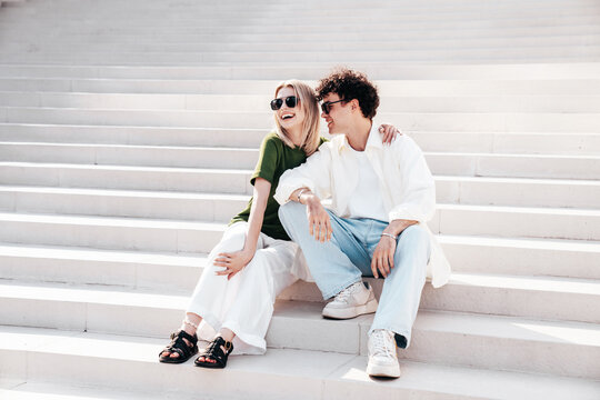 Smiling beautiful woman and her handsome boyfriend. Couple in casual summer clothes. Happy cheerful family. Female and man having fun. They posing in the street in sunny day. Sit at stairs