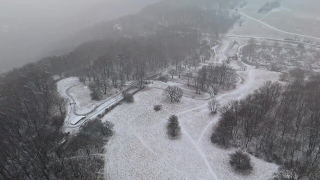 Visegr&aacute;d, Hungary bobsleigh track winding through snow covered forest in the Visegr&aacute;d Mountains during winter snowfall, with closed trails and mountain scenery in aerial view.