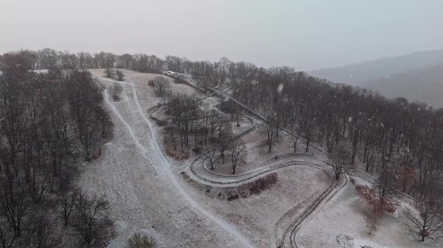 Visegr&aacute;d, Hungary, closed alpine coaster and bobsleigh track winding through snowy forest in the Visegr&aacute;d Mountains during snowfall, winter landscape captured by drone.