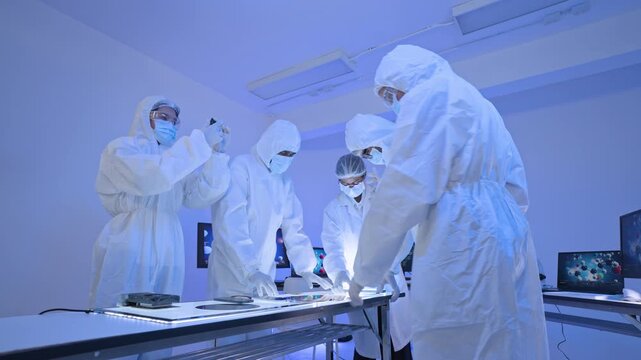 Group of specialists in white protective suits examining wafer discs on illuminated table, semiconductor manufacturing facility, blue light.