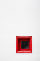 Fototapeta premium minimalist composition featuring a small, square red window frame set deep into a pristine white textured wall. The high contrast creates a bold, modern, and artistic architectural detail.