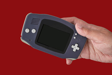 Hand holding retro handheld video game console on isolated red background © punpolpoke