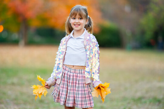 Autumn girl holds foliage. Autumn kid smiles. Colorful autumn portrait. Cute autumn daylight.