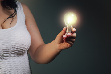 Woman holding a glowing light bulb in her hands on a dark background © Artvibe