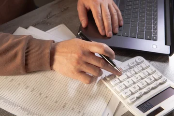 Businessman working with laptop and calculator in office. Close up. © Artvibe