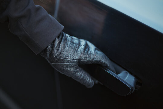 Close up of adult hand wearing glove pulling car door handle, suggesting vehicle access, security or theft. Useful for transport insurance, crime prevention or auto service marketing