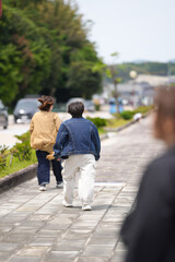Obraz premium Two people stroll down a paved path lined with greenery. One wears a denim jacket, the other a beige coat. They walk away, suggesting a calm, unhurried pace
