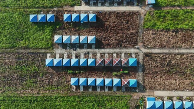 Aerial view of rows of small cabins with blue roofs in a rural landscape.