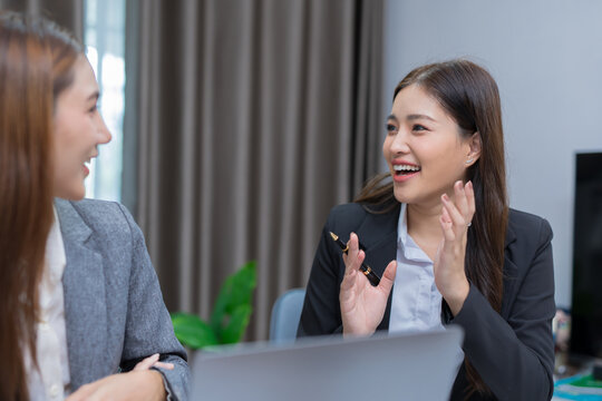 Two professional women work together at a desk, reviewing information on a laptop, collaborating on teamwork and business planning, and analyzing data.