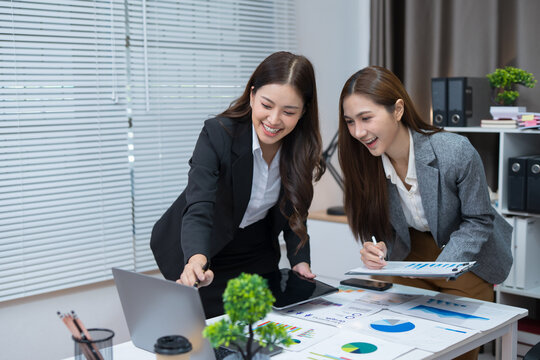  Two professional women work together at a desk, reviewing information on a laptop, collaborating on teamwork and business planning, and analyzing data.