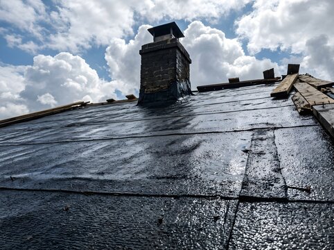 Asphalt roofing felt under construction with chimney against dramatic sky