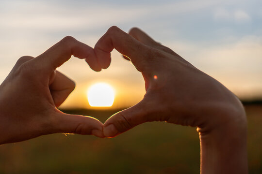Heart shape hands framing golden hour sun outdoors during a peaceful summer evening