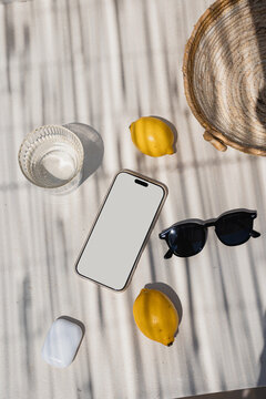 Flat Lay of Summer Essentials. Blank Smartphone Mockup Surrounded By Lemons And Sunglasses In Striped Sunlight