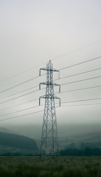 Lone metal pylon ascends a muted sky over expansive rural landscape evoking isolation and quiet strength