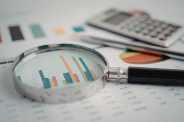 Close-up of a magnifying glass over financial bar charts and graphs with magnifying financial...