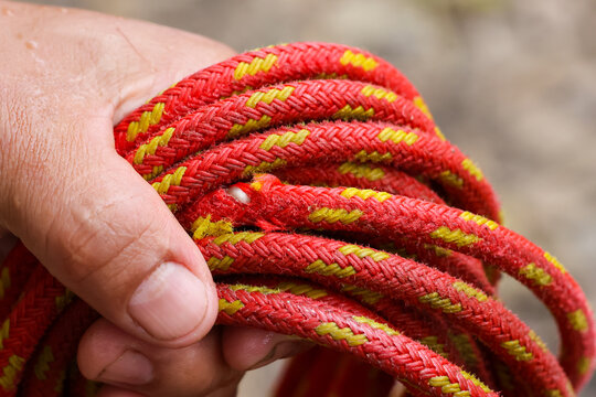 Hand holding coiled red climbing rope with yellow tracer, texture and wear visible, outdoor gear ready for use