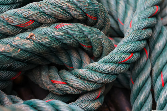 Thick twisted green rope with red twine accents coiled in textured pile, showing frayed fibers and weathered wear, evoking rugged maritime utility and tactile detail