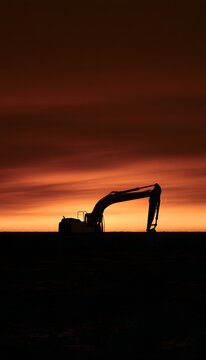 Powerful excavator silhouette against a vast golden sunset landscape evokes industry's strength