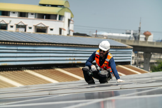 A construction worker carefully installs solar panels on a rooftop in a bustling urban setting surrounded by city buildings