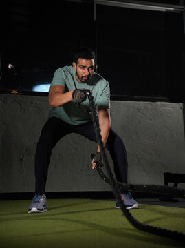 Maharashtra, Sion, India- 22nd March 2026-Young athletic man performing battle rope exercises during a high-intensity functional fitness workout in a modern gym. 