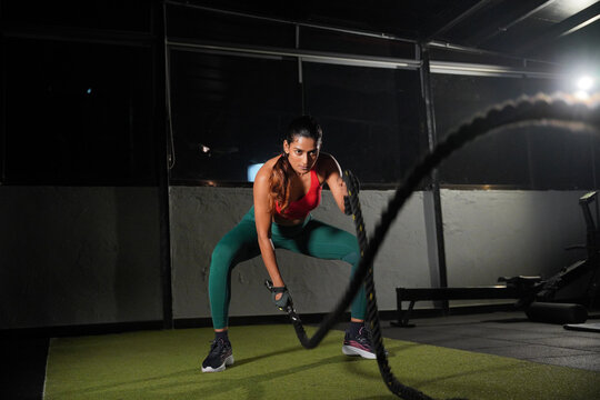 Maharashtra, Sion, India- 22nd March 2026-Athletic young Indian woman performing battle rope exercises in a modern gym during an intense functional fitness workout. 